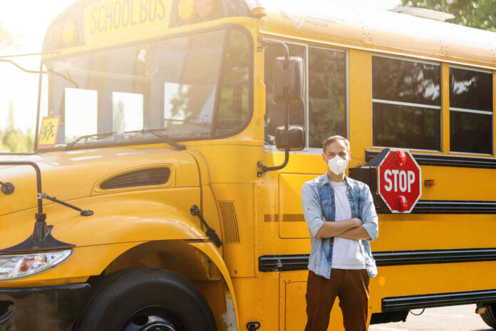 Masked,Bus,Driver,Looking,At,Camera,Outside,The,Elementary,School