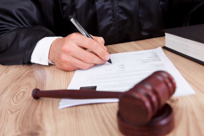 Male,Judge,Writing,On,Paper,In,Courtroom