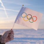 Olympic ICON Breaks Ranks—Stuns Liberal Sports World A hand holding an Olympic flag against a snowy landscape during sunset