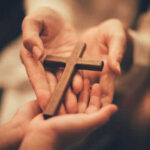 Christian Father Faces Death — Shocking Blasphemy Charge Hands holding a wooden cross together
