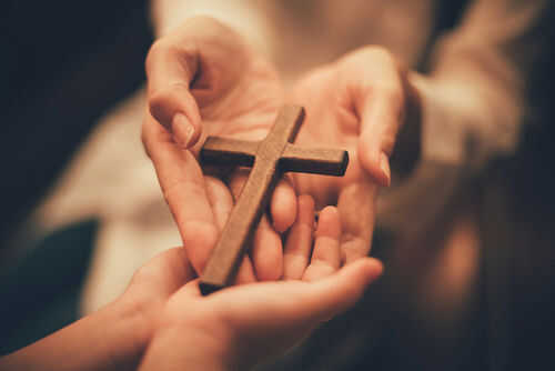 Hands holding a wooden cross together