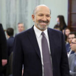Commerce Secretary’s SHOCKING Epstein Ties Exposed Man smiling in a suit at crowded indoor event