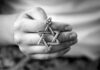 A hand holding a silver Star of David pendant