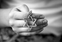 A hand holding a silver Star of David pendant