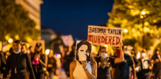 Protesters holding signs and a portrait of Breonna Taylor during a nighttime march