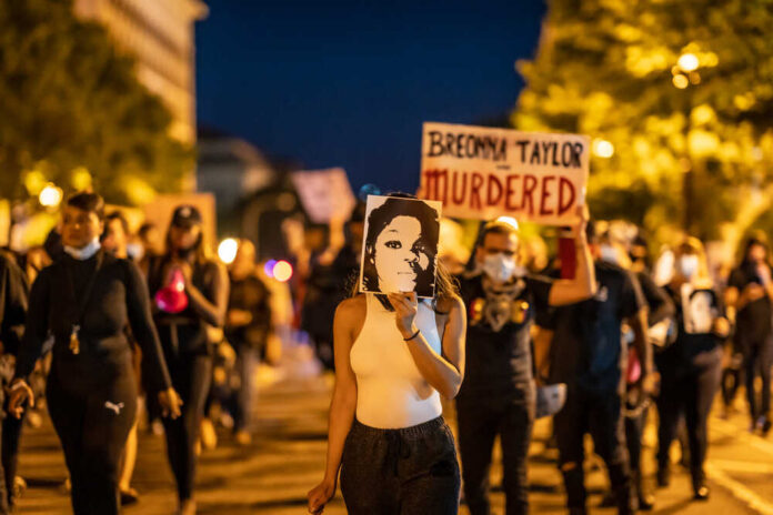 shutterstock_1821332993.jpg Protesters holding signs and a portrait of Breonna Taylor during a nighttime march