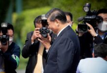A public figure surrounded by photographers at an outdoor event