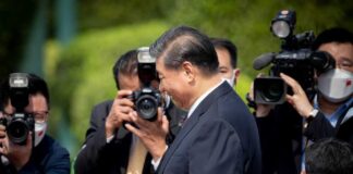 A public figure surrounded by photographers at an outdoor event