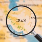 U.S. Casualties Mount – Is Iran War Justified? A magnifying glass focusing on the country Iran on a map