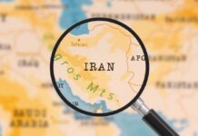 U.S. Casualties Mount – Is Iran War Justified? A magnifying glass focusing on the country Iran on a map