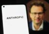 Close-up of a smartphone displaying the word 'ANTHROPIC' with a blurred portrait in the background