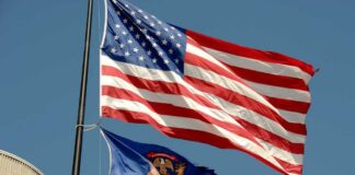 American flag and Michigan state flag flying against a blue sky