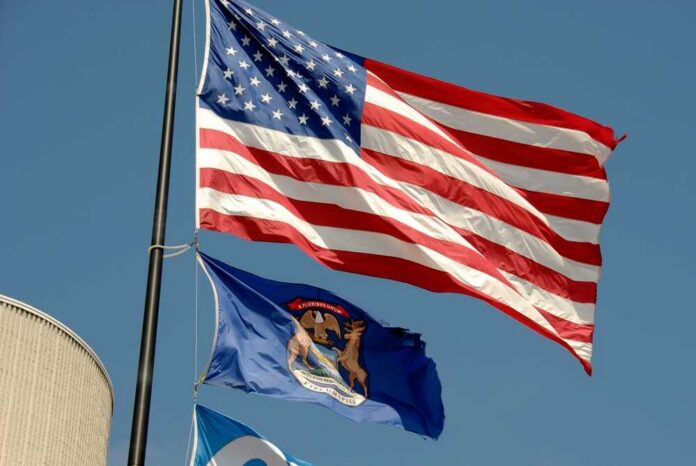 American flag and Michigan state flag flying against a blue sky