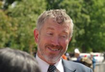 A smiling man in a suit engaging in conversation outdoors