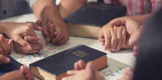 People holding hands with Bibles on table