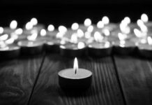 Single candle burning among many on wooden surface.