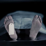 Feet with tag under white sheet in morgue