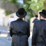 Two men in traditional black attire and hats walking down a street