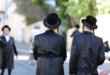 Two men in traditional black attire and hats walking down a street