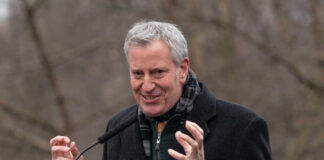 A man in a black coat speaking passionately at an outdoor event