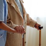 A caregiver holding hands with an elderly person using a cane