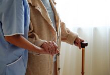 A caregiver holding hands with an elderly person using a cane