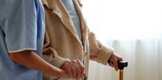 A caregiver holding hands with an elderly person using a cane