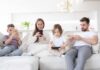 A family of four sitting on a sofa, each using a mobile device