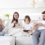 A family of four sitting on a sofa, each using a mobile device