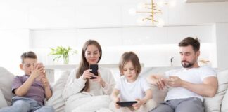 A family of four sitting on a sofa, each using a mobile device