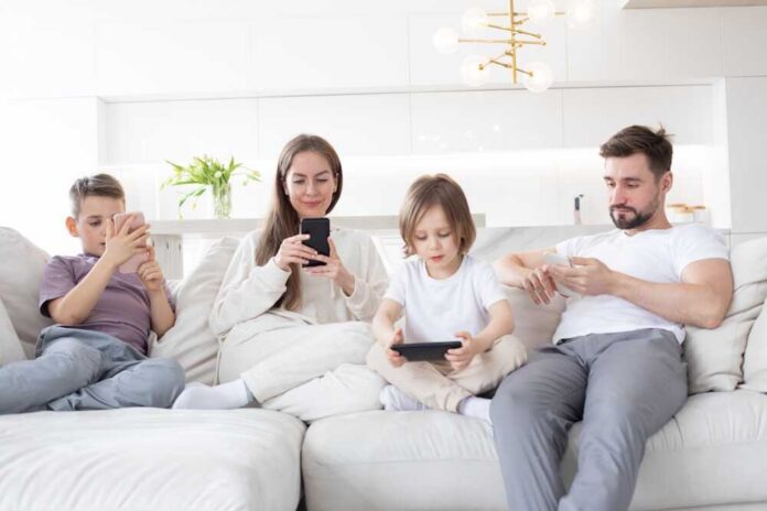 A family of four sitting on a sofa, each using a mobile device