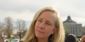 A woman with blonde hair speaking outdoors with a building in the background