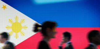 Silhouettes of people walking in front of the Philippine flag