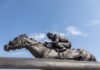 Bronze statue of a jockey riding a horse named Barbaro against a blue sky