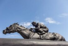 Bronze statue of a jockey riding a horse named Barbaro against a blue sky