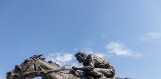 Bronze statue of a jockey riding a horse named Barbaro against a blue sky