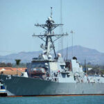 Navy ship docked at harbor with mountains behind