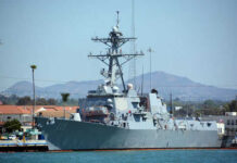 Navy ship docked at harbor with mountains behind