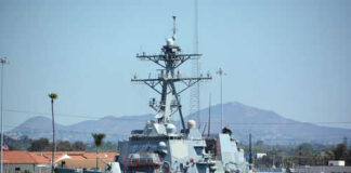 Navy ship docked at harbor with mountains behind