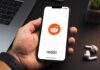 Hand holding smartphone displaying Reddit app logo