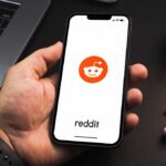 Hand holding smartphone displaying Reddit app logo
