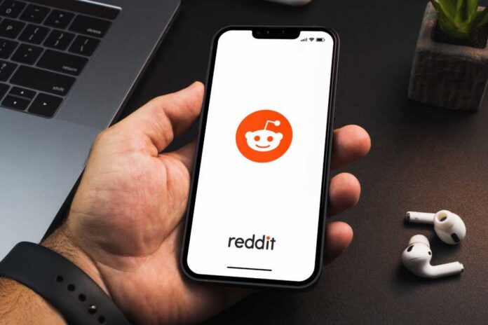 Hand holding smartphone displaying Reddit app logo