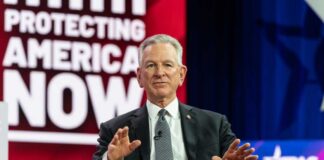 Man in suit speaking on stage with hands raised