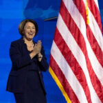 Person clapping near American flag on stage.