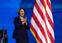 Person clapping near American flag on stage.