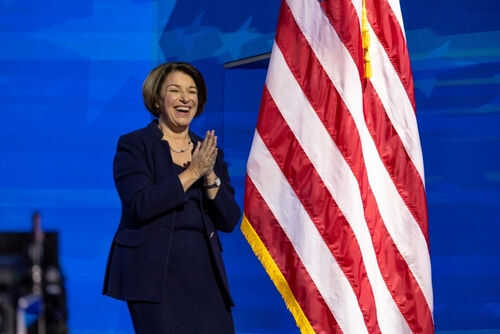 Person clapping near American flag on stage.