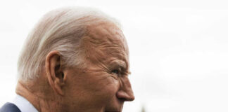Elderly man in profile with grey hair outdoors.