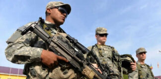 Soldiers in uniform holding weapons outdoors on sunny day