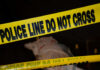 Police tape with indistinct body underneath in shadowed area