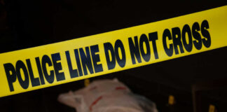 Police tape with indistinct body underneath in shadowed area